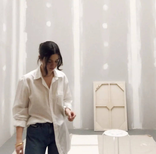 Julia stands in her studio, wearing a long white blouse.