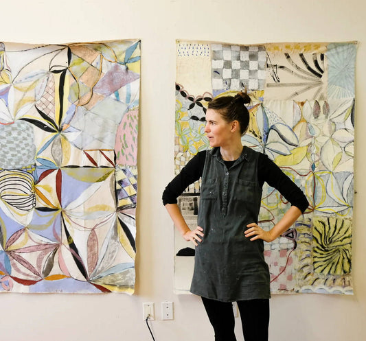 Rachel stands in front of two large pieces of her artwork. 