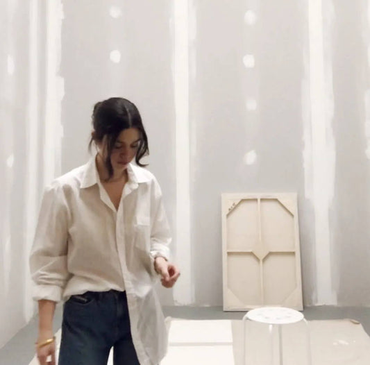Julia stands in her studio, wearing a long white blouse. 